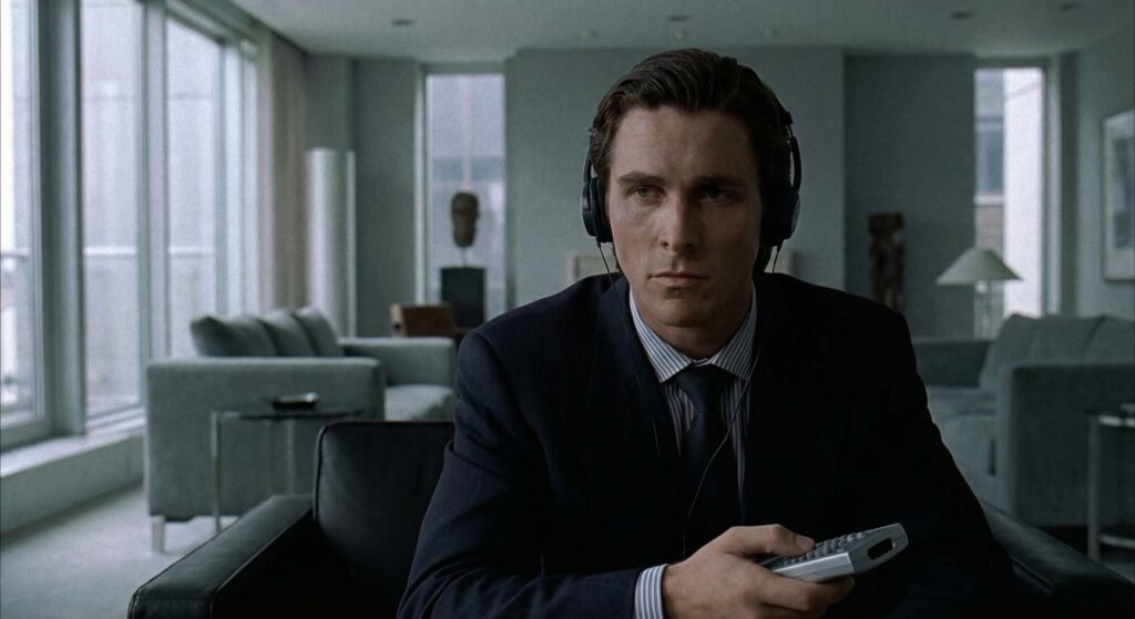 A still image of Patrick Bateman (Christian Bale) from "American Psycho", looking serious and thoughtful, with headphones on.